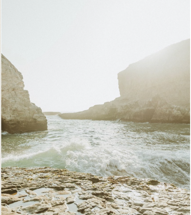 Misty coastal cove with waves breaking between pale sea cliffs